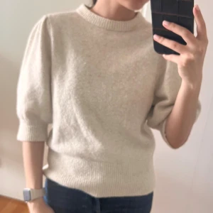 Beige stickad tröja med puffärm - Superfin beige stickad tröja med puffiga halvlånga ärmar och ribbade muddar. Tröjan har en rund halsringning och är perfekt för lager-på-lager under hösten eller våren. Enkel att styla med både jeans och kjol.