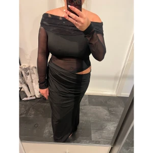 Svart mesh långklänning offshoulder - Säljer en svart långklänning med offshoulder och meshdetaljer. Klänningen har långärmade transparenta ärmar och en cool cut-out vid midjan. Materialet är stretchigt och följsamt, vilket ger en slim passform. Perfekt för dig som gillar trendiga och unika plagg. Passar storlek M/L