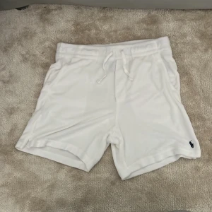 Vita shorts från Polo Ralph Lauren - Säljer ett par vita shorts från Polo Ralph Lauren med snörning i midjan och broderad logga på benet. De har en bakficka och är gjorda i mjuk frotté, perfekta för chill dagar. Helt nytt skick, aldrig använda och pris kan diskuteras!