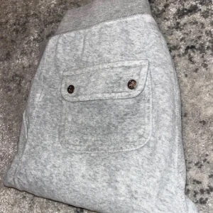 Grå mjukisbyxor från Juicy Couture - Snygga grå mjukisbyxor från Juicy Couture med broderad JC-logga framtill. Byxorna har bred resår och snörning i midjan samt stora fickor med knappar bak. Perfekta för en chill och avslappnad stil. Säljer då dom är för små