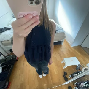 Mörkblå volangig blus - Säljer en mörkblå blus med volanger och hög hals. Toppen är ärmlös och har en luftig, flowy passform med flera lager tyg. Aldrig använd endast provad💓