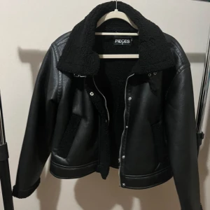 Svart teddyjacka från Pieces XS - Anvönd 1 gång. Säljer en svart teddyjacka från Pieces i storlek XS. Jackan har en stor krage, mjukt teddyfoder och detaljer i skinnimitation. Dragkedja framtill och två fickor med teddy på utsidan. Perfekt för kalla dagar och riktigt snygg stil.