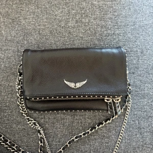 Svart axelväska Zadig & Voltaire skinn - Cool svart axelväska i äkta skinn från Zadig & Voltaire. Väskan har silverfärgade kedjor, nitar längs kanterna, dragkedja bak 