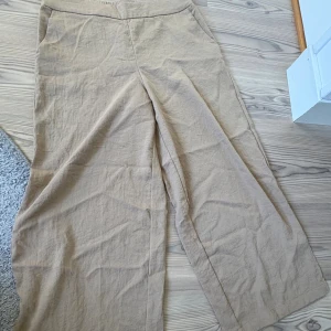 Beiga vida linnebyxor med fickor - Säljer ett par beiga linnebyxor med breda ben och hög midja. Byxorna har resår baktill i midjan och både sidofickor och bakfickor. Perfekta för en chill och avslappnad stil under varmare dagar.