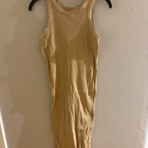 Beige ribbad långklänning - Snygg beige långklänning med ribbad struktur och ärmlös design. Klänningen har en rund halsringning och sitter tight mot kroppen för en slim och modern look. Perfekt för dig som gillar minimalistisk stil och vill ha något enkelt men ändå trendigt.