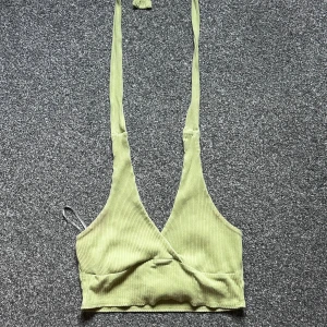 Ljusgrön ribbad croppad linnetopp - Trendig ljusgrön croppad linnetopp med djup v-ringning och långa knytband i nacken. Toppen är ribbad och har omlott-design framtill, perfekt för en cool och avslappnad stil.