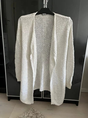 Vit glittrig kofta från Lindex - Säljer en öppen, långärmad kofta från Lindex i vit färg med diskreta glittriga inslag. Koftan är stickad i bomullsmix och har en avslappnad passform som passar perfekt till lager på lager. Materialet är 95% bomull och 5% metallfiber. St.170, passar även S