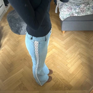 Ljusblå bootcut jeans med spetsdetalj - Säljer ett par ljusblå bootcut jeans med snygg vit spets längs sidorna. Jeansen har låg midja med två knappar och inga fickor💓💓. 