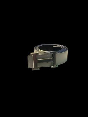 Vändbart vitt och svart bälte med H-spänne - Säljer ett stilrent vändbart bälte i vitt och svart med ett stort H-format metallspänne. Bältet är i slätt material på den vita sidan och har en mer texturerad yta på den svarta sidan. Perfekt accessoar för att lyfta din outfit.