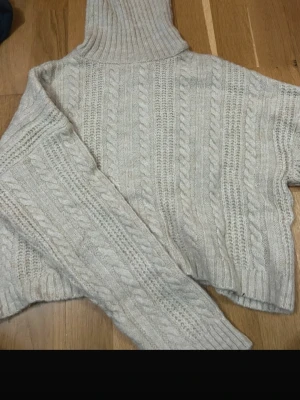 Beige polotröja från Stradivarius - Säljer en beige polotröja från Stradivarius i storlek S. Tröjan är stickad med klassiskt flätmönster och har en hög, ribbad polokrage samt långa ärmar. Perfekt för kyliga dagar och superenkel att styla till jeans eller kjol.