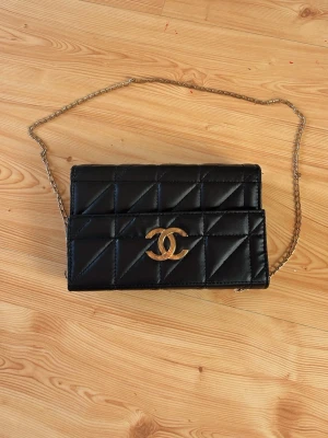 Svart CC väska  - Säljer en svart quiltad axelväska från CC med klassiskt guldigt CC-spänne och kedjerem. Väskan har en elegant och tidlös design med rutmönster och är tillverkad i skinn. Perfekt för dig som vill ha en ikonisk accessoar med lyxig känsla.
