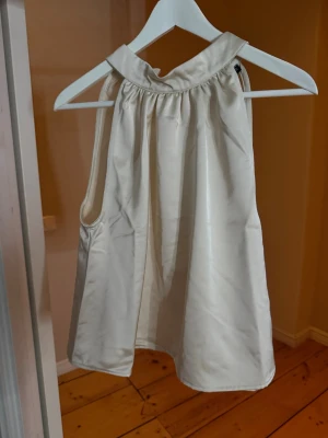 Vit halterneck linnetopp i satin - Säljer en elegant vit linnetopp i satin med halterneck och knäppning i nacken. Toppen är ärmlös och har en lös passform som faller snyggt. Helt ny, prislapp kvar 🌟 Nypris 499kr