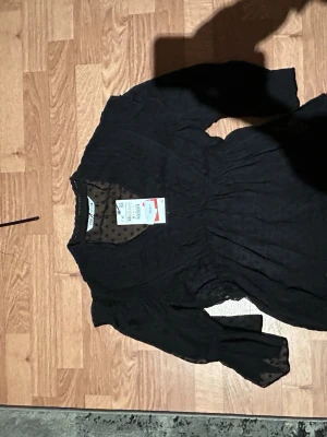 Svart prickig blus/topp från Zara - Supersnygg svart blus/topp från Zara med transparenta ärmar och prickigt mönster. Blusen har v-ringning och lätt puffade långärmar som ger en trendig look. Perfekt för dig som vill ha något stilrent men ändå lekfullt.
