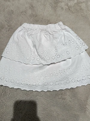 Vit volangkjol från Zara - Supersöt vit kjol från Zara med dubbla volanger och broderade blommönster. Kjolen har resår i midjan och är gjord i mjuk bomull. Perfekt för sommarens alla dagar och ger en fräsch och romantisk vibe. Själv har jag aldrig använt den utan den har legat i min garderob. Dock så är den jätte liten för mig för jag är äldre nu