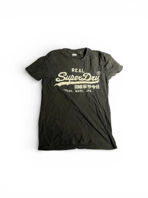 Svart Superdry t-shirt med tryck - Svart t-shirt från Superdry med stort vitt tryck på bröstet och japansk text. Klassisk rund hals och korta ärmar. Tillverkad i mjuk bomull som känns skön mot huden. Perfekt för en avslappnad och cool stil.