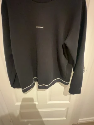 Svart sweatshirt från Emporio Armani - Säljer en svart sweatshirt från Emporio Armani med diskret logga på bröstet och vita detaljer längs nederkanten. Tröjan har rund halsringning och långa ärmar, perfekt för dig som gillar stilren och enkel design.