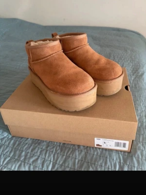 UGG bruna plattform boots mocka - Säljer ett par bruna UGG boots i mocka med chunky plattformsula. Skorna har rund tå och är fodrade med mjukt material på insidan. Perfekta för höst och vinter när du vill ha både stil och värme. Klassisk UGG-look fast med modern twist tack vare den höga sulan.