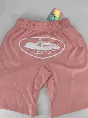 Cortez  - Säljer ett par rosa shorts från cortez med vitt tryck av ett fartyg på framsidan. Shortsen har elastisk midja och avslappnad passform, perfekta för sommardagar. Tillverkade i mjuk bomull för maximal komfort. Den är använd i en kort tag 
