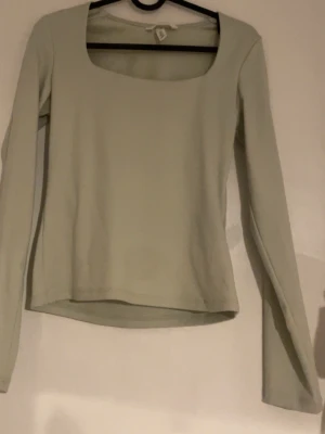 Ljusgrön långärmad topp från H&M - En stilren ljusgrön långärmad topp från H&M i storlek S. Toppen har en fyrkantig urringning och är gjord i ett mjukt, stretchigt material som sitter bekvämt. Perfekt att matcha med jeans eller kjol för en clean look.