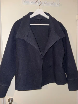 Mörkblå kappa - Säljer en mörkblå kappa med knäppning framtill. Jackan har en loose passform och långa ärmar, perfekt för kyligare dagar. Enkel och stilren design som funkar till många outfits.