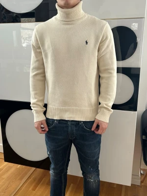 Polo Ralph Lauren tröja  - Säljer en stilren vit polotröja från Polo Ralph Lauren i storlek L. Tröjan är ribbstickad i mjuk bomull, har lång ärm och klassisk polokrage. Den ikoniska lilla loggan är broderad på bröstet. Perfekt för dig som gillar en clean och tidlös look.