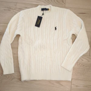 Vit Polo Ralph Lauren knit - Vit kabelstickad tröja från Polo Ralph Lauren med klassisk rund hals och broderad logga på bröstet. Tröjan är i 100% mjuk bommul.                                📏Storlek M.                                                   ⭐Oanvänd i perfekt skick med tagg.