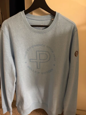 Ljusblå sweatshirt från Pelle P - Sweatshirt i ljusblått från Pelle P med rund hals och tryckt logga på bröstet. Använd enstaka gång och nästan som ny därav priset…!
