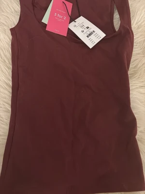 Vinröd topp från Gina Tricot - Säljer en basic vinröd linnetopp från Gina Tricot, modell elevated basics. Toppen har en fyrkantig halsringning och är ärmlös med en slim passform. Perfekt att styla med jeans eller kjol. Färgen heter Tawny port och materialet är stretchigt. Helt ny och ej använd bara testad EN gång men säljer pga för liten för mig! Pris kan diskuteras