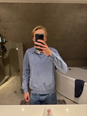 Ljusblå pikétröja med lång ärm - Säljer en stilren ljusblå pikétröja med lång ärm och klassisk krage. Tröjan har knappar vid halsen och är tillverkad i ett mjukt material som känns skönt mot huden. Perfekt för dig som gillar en clean och enkel look. Jag på bilden är 183 cm