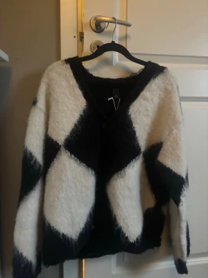 Svartvit rutig kofta från Monki - Fluffig kofta från Monki i svart och vitt med stort rutigt mönster. Koftan har v-ringning, knappar framtill och är långärmad. 