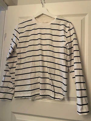 Vit och svart randig långärmad topp - Säljer en klassisk långärmad topp med svarta horisontella ränder på vit botten. Toppen har rund halsringning och är gjord i mjuk bomull, perfekt för en enkel och stilren look.