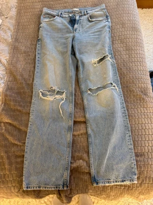 Ljusblå straight gina jeans  - Säljer ett par ljusblå jeans med raka ben och stora slitningar på båda benen. Inga skador, väldigt fina! 