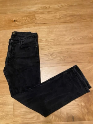 Svarta Lee jeans straight fit - Säljer ett par svarta jeans från Lee med klassisk femficksdesign och raka ben. Jeansen har normal passform och är tillverkade i slitstarkt denimtyg. Perfekta för dig som gillar en enkel och tidlös look.