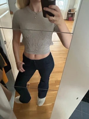 Glittrig croppad topp med öppen rygg - Säljer en ljusglittrig croppad topp med korta ärmar och snyggt mönster framtill. Toppen har öppen rygg med knytband som ger en unik look. Perfekt till dig som vill sticka ut lite extra.