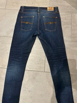 Nudie Jeans Lean Dean blå jeans 32/32 - Säljer ett par Nudie Jeans Lean Dean i mörkblå tvätt med klassiska kontrastsömmar och snygga bakfickor med broderad detalj. Modellen är slim med rak passform och tillverkad av 99% ekologisk bomull och 1% elastan för lite stretch.