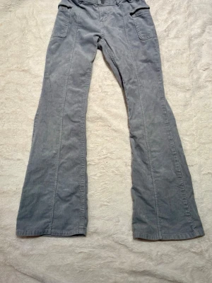 Gråblå manchesterbyxor från Lindex - Säljer ett par ljusblå manchesterbyxor från Lindex med bootcut-modell. Byxorna har stora fickor fram och bak, dubbla knappar i midjan och justerbar resår. Perfekta för dig som gillar retrovibbar och mjukt material.