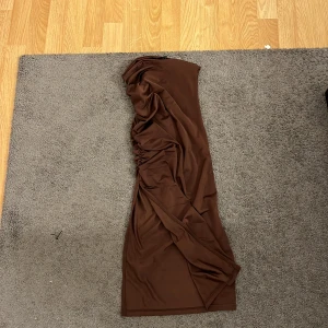 Brun långklänning i XS - Snygg brun långklänning i storlek XS med draperade detaljer längs sidan. Klänningen är ärmlös och har en mjuk, stretchig känsla i materialet. Perfekt för dig som gillar minimalistisk stil och jordnära färger.