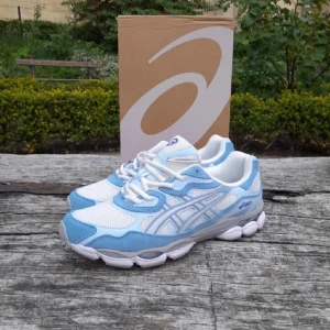 Asics nyc - Snygga Asics Gel sneakers i vitt och ljusblått med grå detaljer. Ovandelen är i mesh och syntet med klassiska Asics-ränder på sidorna. Skorna har snörning, rund tå och en chunky vit sula med gel-dämpning för extra komfort. Perfekta för dig som gillar sportig stil.