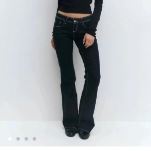 Mörkblå bootcut jeans med kontrastsömmar - Säljer ett par mörkblå jeans med låg midja och tydliga vita kontrastsömmar. Modellen har bootcut-ben och klassisk femficksdesign. Jeansen är i ett stretchigt denimtyg som sitter snyggt och markerar siluetten. Nypris 400, med prislappen på, endast testad!