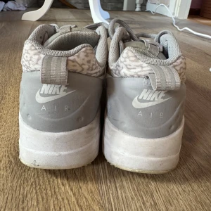 Nike Air sneakers i ljusgrått mönster - Nike Air sneakers i storlek 37.5 med ljusgrå och vit färgton. Skorna har ett unikt mönster på ovandelen, rund tå, snörning och synlig Air-dämpning i sulan. Materialet är syntet och textil, och de har en platt sula för skön komfort.
