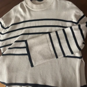 Randig stickad tröja i beige och svart - Säljer en snygg stickad tröja med breda bruna ränder på beige botten. Tröjan har rund hals, långa ärmar och ribbade muddar samt nederkant. Perfekt för lager-på-lager och chill höststil.