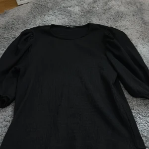 Svart långärmad topp från Missay - En svart långärmad topp från Missay med rund halsringning och lätt puffade axlar. Tyget har en diskret struktur som ger en snygg touch. Perfekt att styla med jeans eller kjol för en clean look.