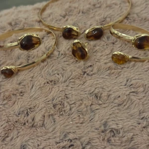 Halsband,ring 1 överarms armband och 1 handledarmband i KC-guldpläteradmed bruna stenar - Säljer ett set med två guldpläterad armband och en matchande ring och halsband alla med unika bruna stenar i oregelbunden form. Armbanden är öppna och har två stenar vardera, medan ringen har en större sten. Perfekt för dig som gillar boho och statement-smycken.