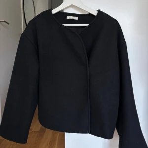Kappa - Svart kappa från Gina med rundad hals. Det finns dolda knappar, man knäpper jackan på sidan. Superfin🥰storlek S