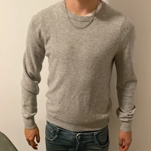 Ljusgrå stickad tröja  - Snygg ljusgrå stickad tröja från Maglia Studio. Tröjan har rund hals, ribbade muddar och lång ärm. Perfekt för dig som gillar stilrena och enkla plagg. Passformen är normal och materialet känns mjukt och skönt mot huden.