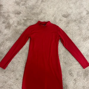 Röd långärmad klänning från SHEIN - En enkel och stilren röd klänning från SHEIN med lång ärm och hög krage. Modellen är kroppsnära och har en rak siluett som slutar ovanför knäna. Perfekt för dig som gillar minimalistisk stil och vill sticka ut med färg. Klänningen är aldrig använd den är endast prövad en gång.