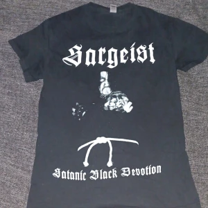 Sargeist svart band t-shirt - Svart t-shirt med tryck från Sargeist och texten 'Satanic Black Devotion' på framsidan. Baksidan har ett stort svartvitt skogsmotiv och texten 'Returning To Misery & Comfort'. Klassisk passform och crewneck, perfekt för dig som gillar black metal.