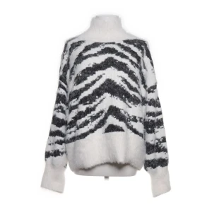 Vit och svart zebramönstrad polotröja - Fluffig polotröja i vit och svart med zebramönster. Tröjan har en hög krage, långärmade ärmar och loose passform. Materialet är stickat och känns mjukt och cozy, perfekt för kyliga dagar. Snyggt mönster som sticker ut och ger en cool vibe. Liten i storleken