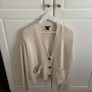 Beige ribbad kofta från Lindex - Säljer en beige ribbad kofta från Lindex i storlek S. Koftan har v-ringad hals, tre stora knappar framtill och två praktiska fickor. Den är långärmad och har en loose passform som gör den extra chill. Perfekt att slänga på sig när det är lite kyligt ute. Den är perfekt för vintern och är en skit snygg kofta som passar till allt. Den kan vara en myströja eller en snygg kofta till jeans.