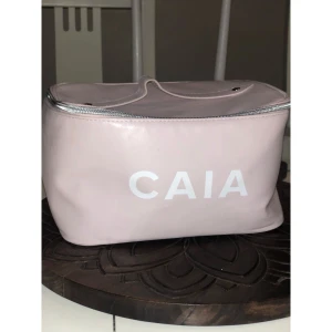 Ljusrosa necessär från CAIA - Söt och rymlig ljusrosa necessär från CAIA med silvrig dragkedja. Väskan är tillverkad i glansigt syntetmaterial och har en stilren, boxig form med CAIA-logga framtill. Perfekt för smink eller hudvård när du är på språng.